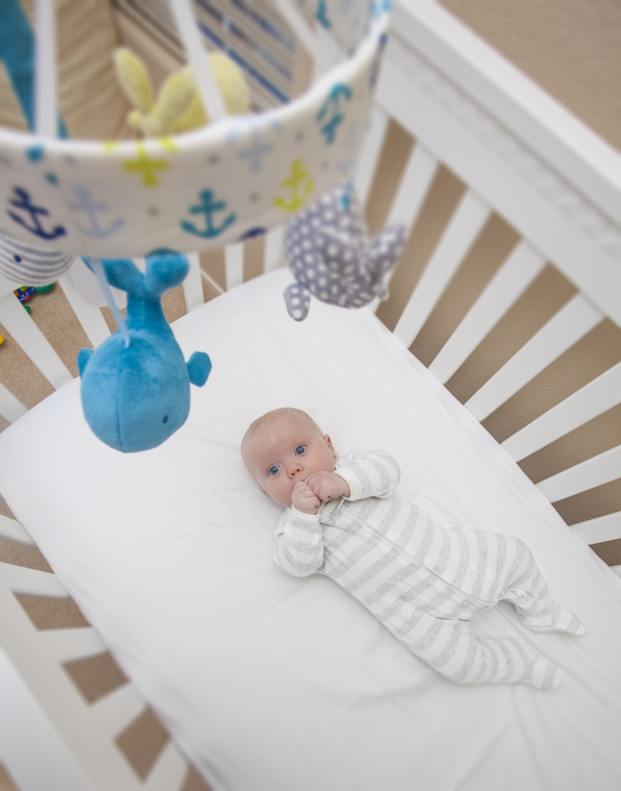 A 3 month old baby boy laying in his crib looking up at a mobile.