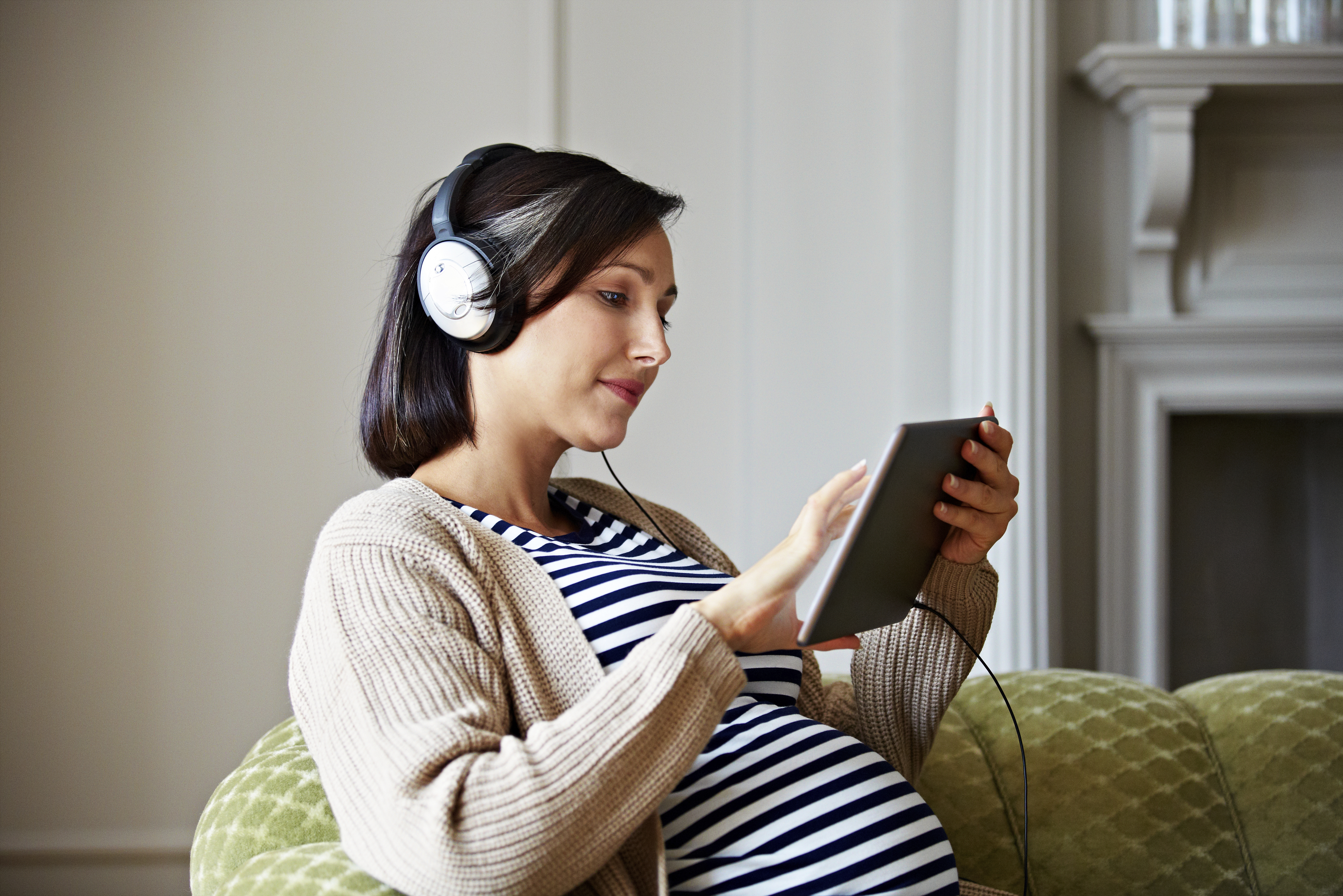 Shot of a pregnant woman sitting on her sofa listening to music on a digital tablet